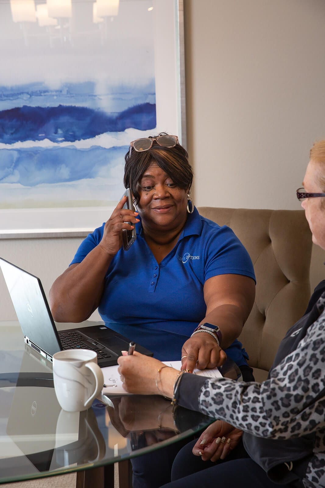 Woman on the phone and laptop helping another woman complete paperwork